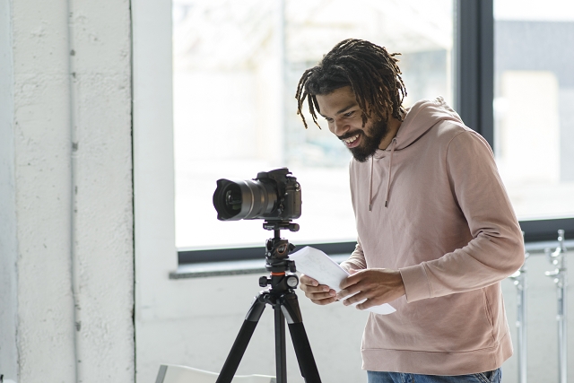 A cheerful man setting up a professional camera on a tripod indoors.