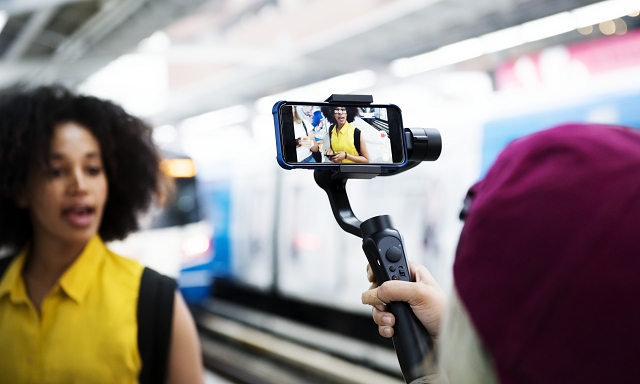 A content creator vlogging in a subway station, with a smartphone camera focused on her.