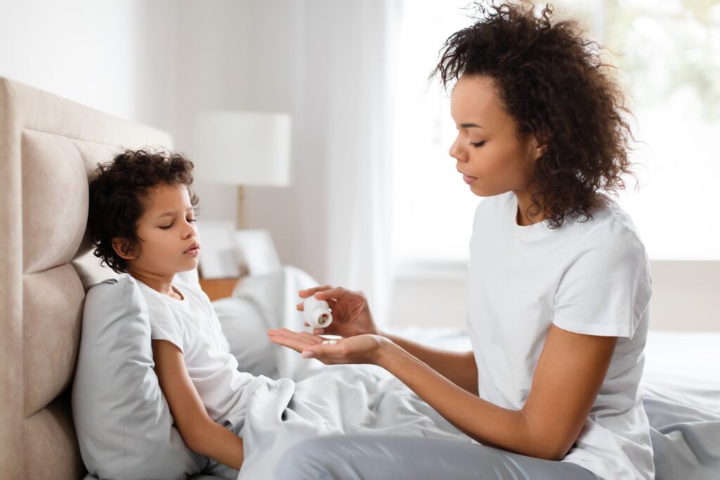 Caring Mother Giving Medicine to Her Sick Child in Bed