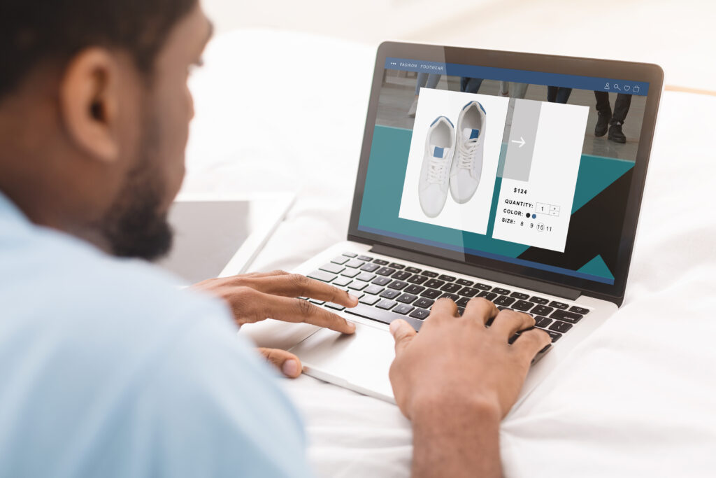 Man browsing sneakers on an e-commerce product page showing price, size and color options on a laptop